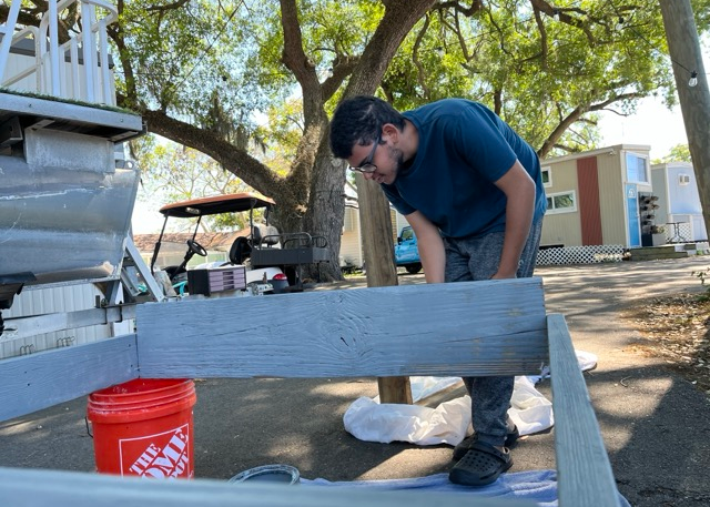 Resident painting wooden garden bed structure in community garden build Resident painting wooden garden bed structure in community garden build